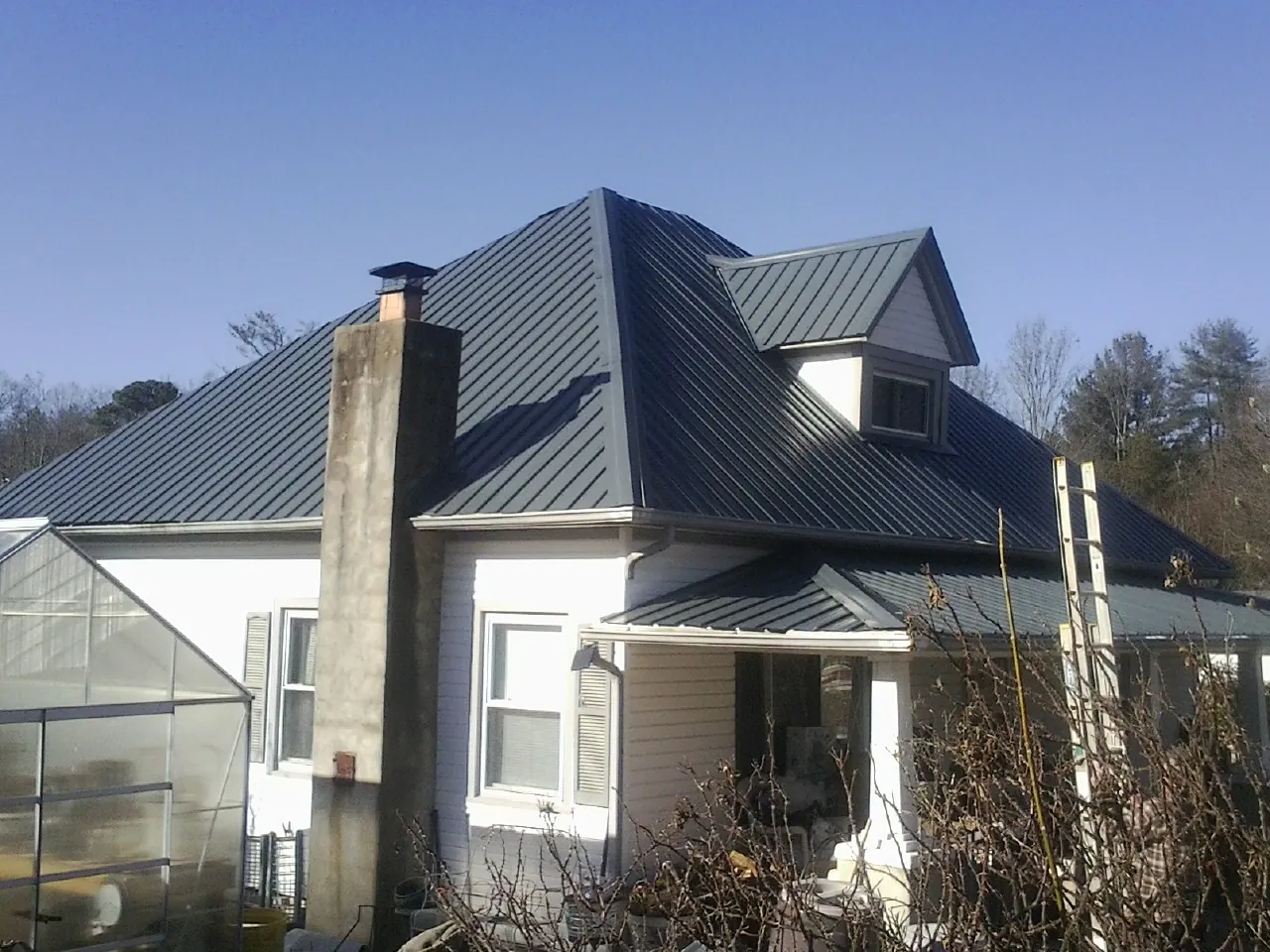 Dark blue standing seam metal roof on a white farmhouse with dormer — Slate & Tile Roof Repair by Roofing Brothers in Dyke