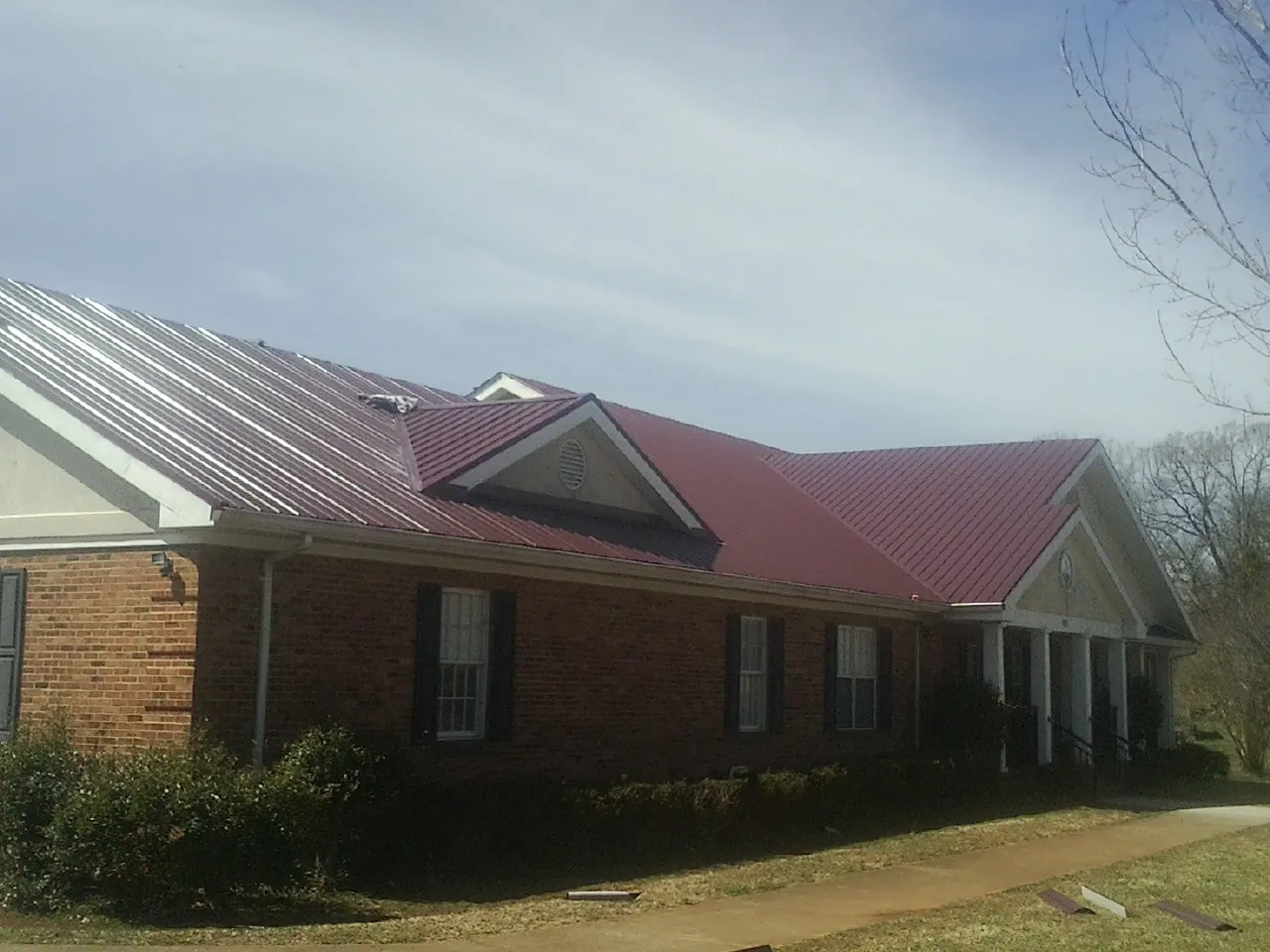 Red metal roof with gabled entries on a long brick building, from a Hail Damage Roof Repair job in Dyke