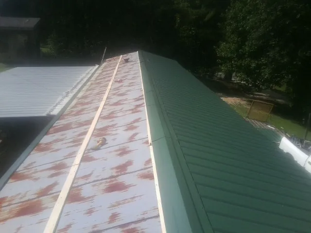 Old rusted panels beside newly installed green metal roofing — Wind Damage Roof Repair by Roofing Brothers in Dyke