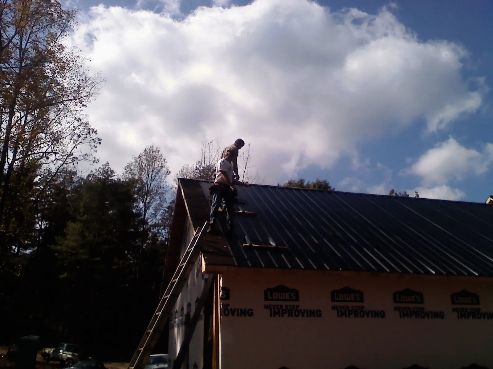 Roofer fastening dark metal panels high against a cloudy sky, from a Roof Inspection job in Dyke