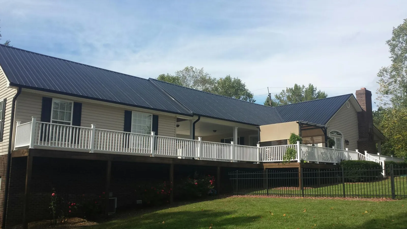 Black metal roof above a long white railed deck on a hillside home in Dyke