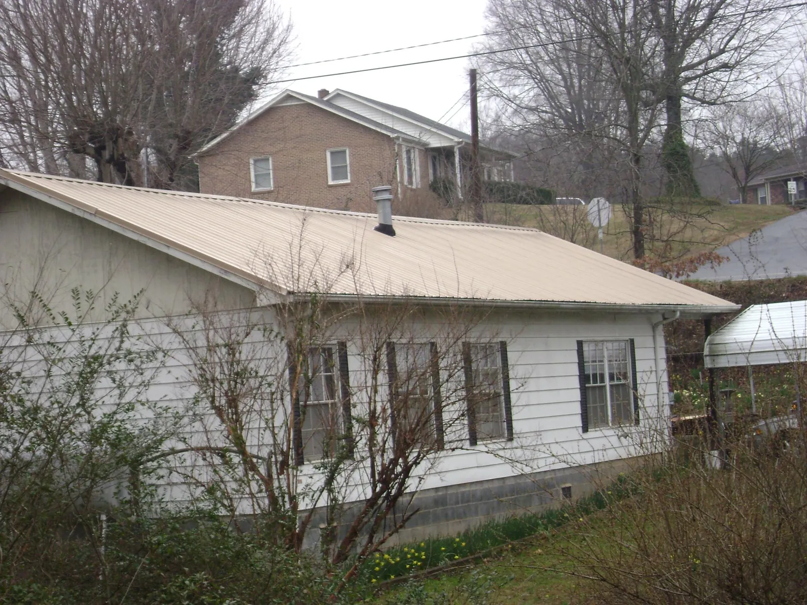 Tan metal roof on a white sided house set into a hillside — Commercial Roofing by Roofing Brothers in Dyke